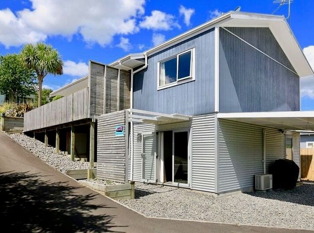 A two-story house with blue and white siding a wooden deck and gravel around the base at Harakeke House Downstairs - Ohakune Unit in Ohakune