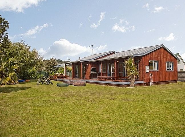 A wooden house with a large grassy yard and outdoor seating at Castleview Getaway Matarangi in Matarangi