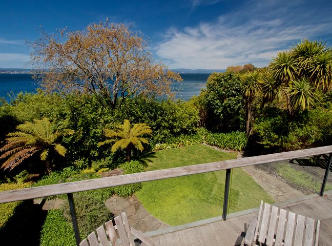 A garden with green grass and trees overlooking a body of water at Kauawhi Lodge - Acacia Bay Holiday Home in Acacia Bay