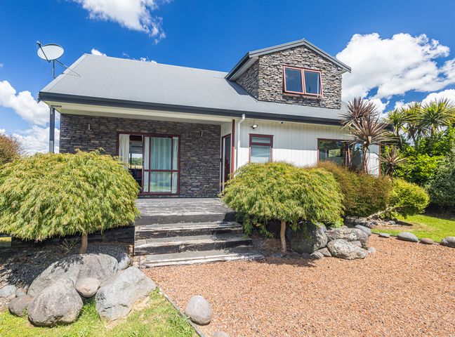 The exterior of a house with stone and white siding surrounded by shrubs and rocks at Willstone Chalet - Ohakune Chalet near Turoa in Ohakune