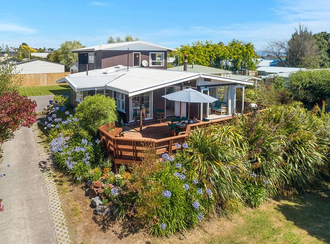 A house with a wraparound wooden deck and umbrella surrounded by plants and flowers at Wharewaka Hideaway Wharewaka