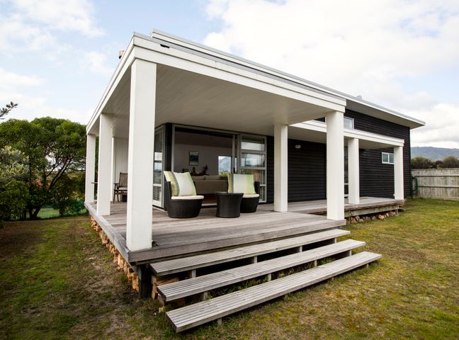 A covered wooden porch with two chairs and a small table outside a modern black house at Waikanae Retreat in Waikanae Beach