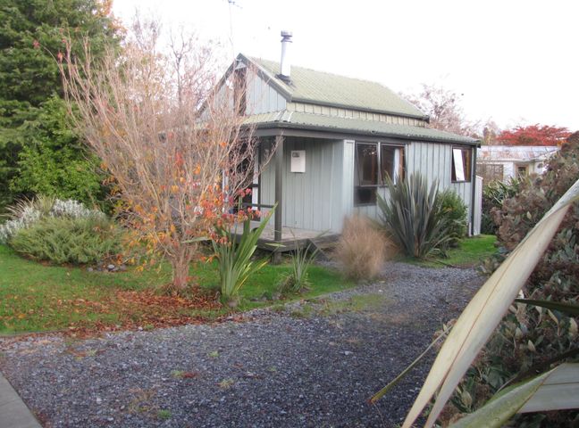 A small house with a green roof surrounded by plants and a gravel driveway at Miro Magic - Ohakune Holiday Home in Ohakune