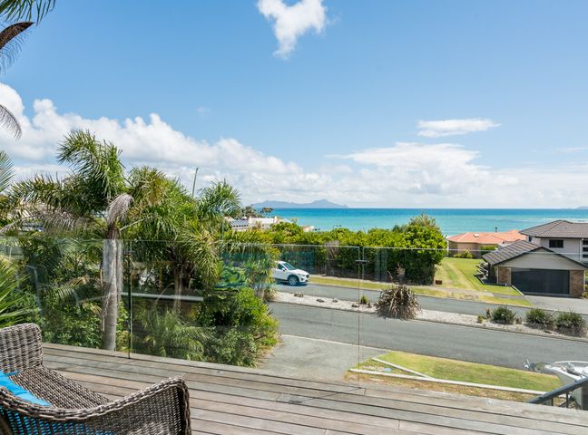 A balcony with a wicker chair overlooking a road trees houses and the ocean at Ocean Oasis  Langs Beach