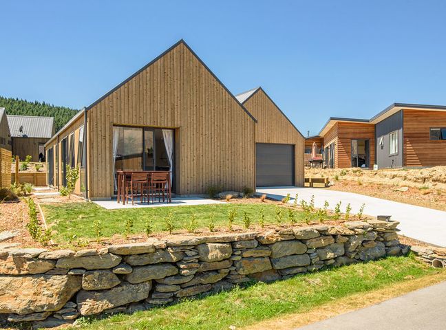 A wooden house with a patio table and chairs and a stone retaining wall at The Place To Be - Wanaka Holiday Home in Wanaka
