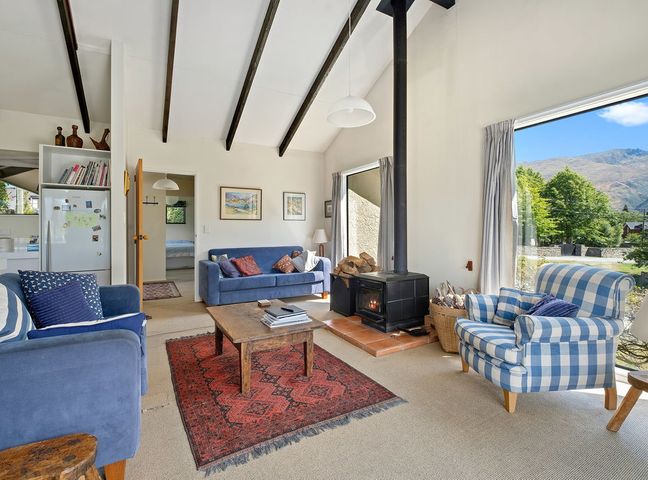 A living room with sofas a wood stove and large windows showing trees and mountains at Southern Serenity Wanaka Holiday Home in Wanaka