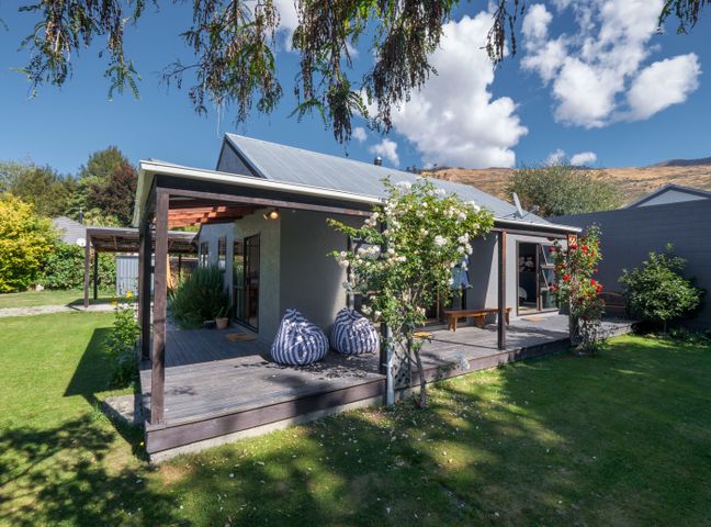 A backyard with a wooden deck attached to a house with two bean bags and flowering plants at Haven on Heuchan Wanaka Holiday Home in Wanaka
