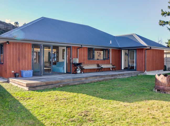 A wooden house with a metal roof a wooden deck with benches and a grill and a grassy yard at GraceWorks - Hanmer Springs in Hanmer Springs