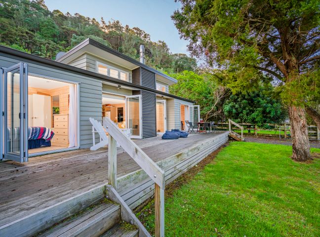 A deck with chairs and a table outside a house with open doors and a grassy yard at Opoutere Oasis Opoutere