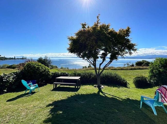 A garden with a tree a picnic table and two blue chairs overlooking a body of water at Henley - Omori Holiday Home in Omori