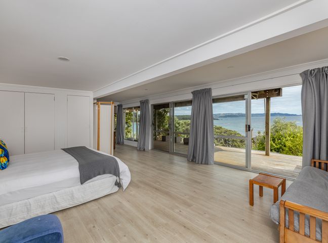 A bedroom with a bed sofa small table and large sliding glass doors overlooking a deck and water at Tapuaetahi Beachfront Studio - Downstairs Unit in Kerikeri