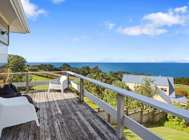 A wooden deck with two white chairs and a black cover with ocean view at Mayor Magic - Onemana Holiday Home in Onemana