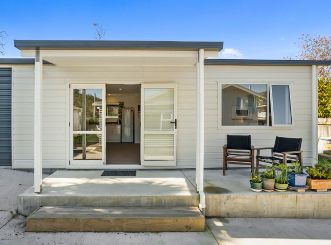 Exterior view of a single-story house with a small porch two chairs and potted plants at Karori Kabin in Karori