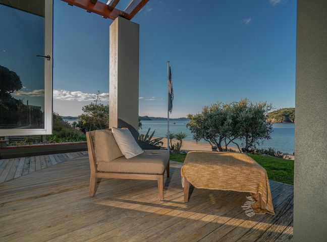 A patio with a cushioned chair and ottoman overlooking the beach and water at Hahei Oceanfront Hahei