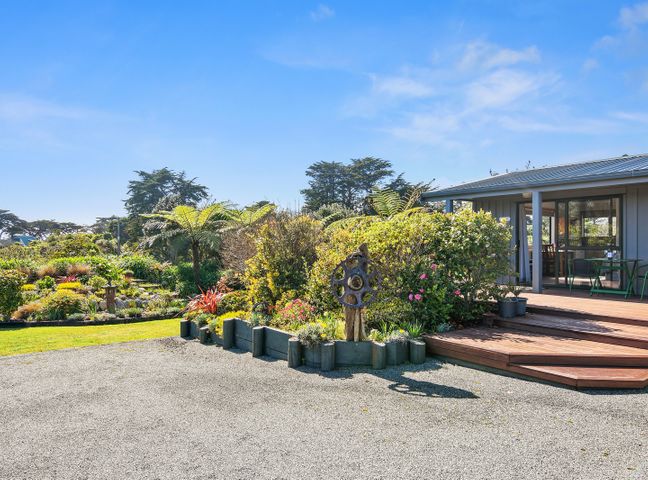 A garden with plants and shrubs next to a wooden decked porch of a house at Upepo - The Garden Room - Cape Foulwind Studio in Cape Foulwind
