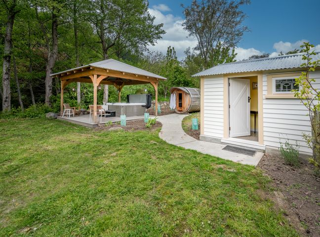 A garden area with a covered hot tub, chairs, a small building with an open door, and greenery at Matagouri Cottage Port Levy Holiday Home