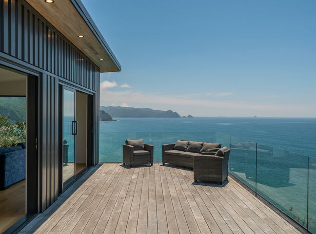 An outdoor deck with wicker seating overlooking the ocean at Purepure - Tairua Holiday Home in Tairua