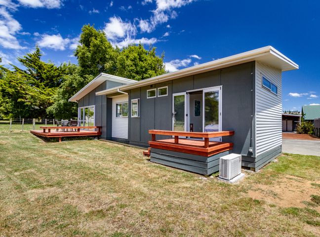 A modern house with wooden decks and sliding glass doors surrounded by grass and trees at Alpine Retreat Ohakune