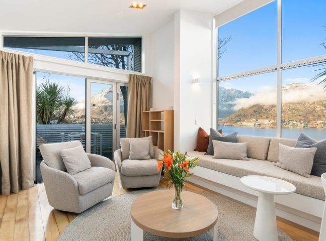 A living room with armchairs sofa coffee table and large windows overlooking mountains and lake at A Stunning Stay Queenstown Holiday Home in Queenstown