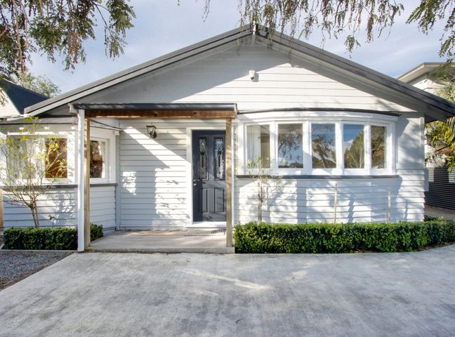 The front exterior of a single story house with a covered porch and black door at Kuku Villa - Te Awanga Holiday Home in Te Awanga