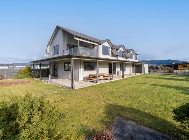 A two-story house with a covered patio and lawn at Acheron Homestead - Te Anau Holiday Home in Te Anau