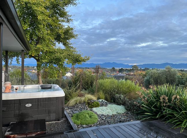 An outdoor space with a hot tub next to a garden and a view of mountains and houses at Views over Blenheim - Blenheim Holiday Home in Blenheim