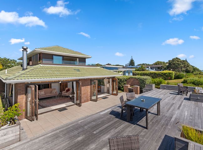 Outdoor patio area with tables and chairs next to a two story house with a green tiled roof at Island View Beach House Paraparaumu Beach