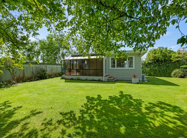 A small house with a screened porch and green lawn surrounded by trees at Carrington Countryside - New Plymouth Holiday Home in Taranaki