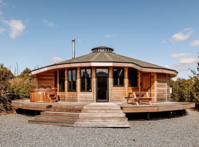 A round wooden cabin with a hot tub on the left and a picnic table on the right at Kaho - Ohakune Holiday Home with Spa in Ohakune