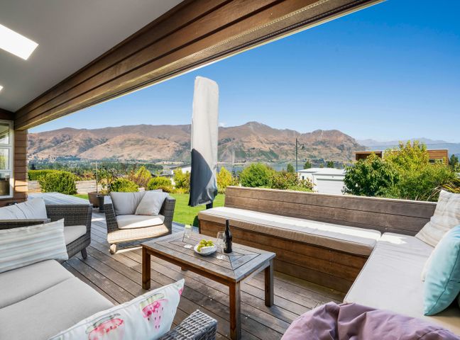 An outdoor patio with cushioned chairs a wooden table and a view of mountains at Lake Vista Retreat Wanaka