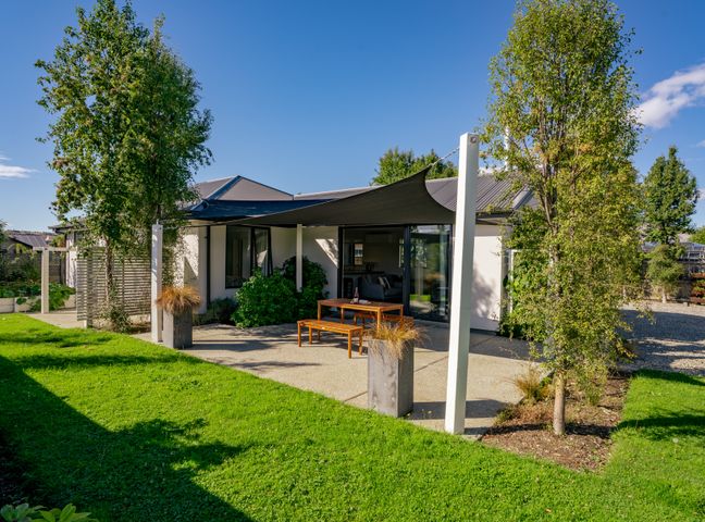 A backyard patio with a wooden table and bench under a shade sail at Relax on Snowberry in Wanaka