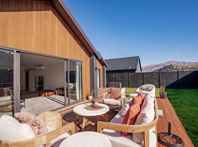 An outdoor wooden deck with sofas chairs a round table and a view of mountains at Wooing Retreat - Cromwell Holiday Home in Cromwell