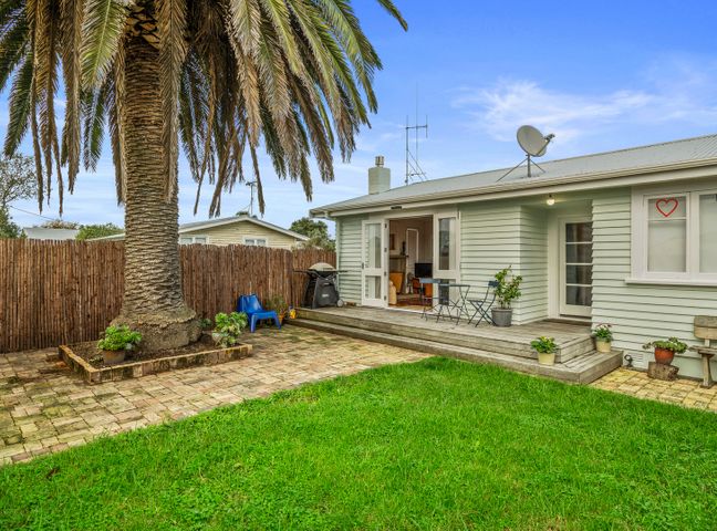 A backyard with a palm tree a patio with chairs a barbecue and plants at The Remodelling Room - Mount Maunganui Cottage in Mt Maunganui