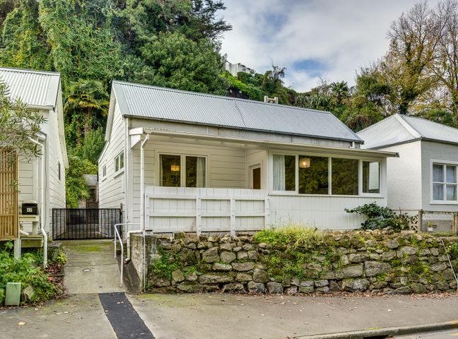 A small white house with a corrugated metal roof stone retaining wall and stairs between houses at Central Cottage Napier