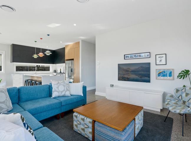 A living room with a blue sofa a wooden coffee table and a white TV stand with pictures on the wall at Stylish Serenity Martinborough