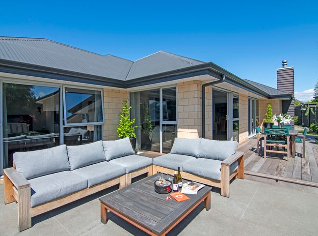 An outdoor patio with gray cushioned wooden sofas and a wooden coffee table with books and bottles at Banksia Retreat - Blenheim Holiday Home in Blenheim