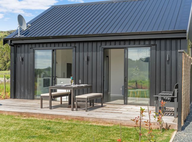 Outdoor wooden deck with table, benches, and chairs attached to a black metal house at Barn 944 - Big Omaha Holiday Home in Big Omaha