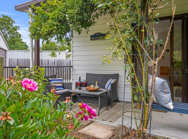 An outdoor seating area with a table, chairs, cushions, and wine glasses surrounded by plants at Rose Cottage - Lake Coleridge Holiday Home in Lake Coleridge