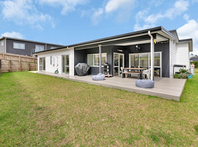 A backyard with grass and a wooden deck attached to a single-story house with outdoor furniture and a barbecue at Seaside Escape - Ruakaka Holiday Home in Ruakaka