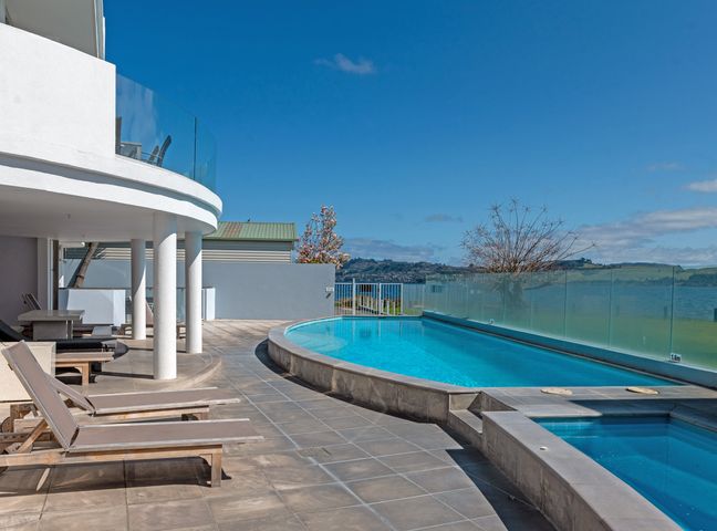An outdoor pool area with lounge chairs and a glass fence overlooking a body of water at Waimahana 5 - Taupo Holiday Apartment in Waipahihi