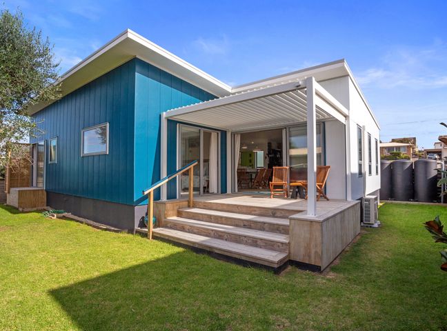 A backyard with a wooden deck and outdoor chairs attached to a modern blue and white house at Serene on Seaforth in Waihi Beach
