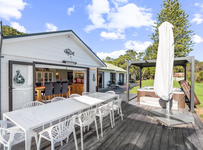 An outdoor wooden deck with a long white dining table with chairs a covered hot tub and lounge chairs outside River Palms Retreat - Paihia Holiday Home in Haruru Paihia