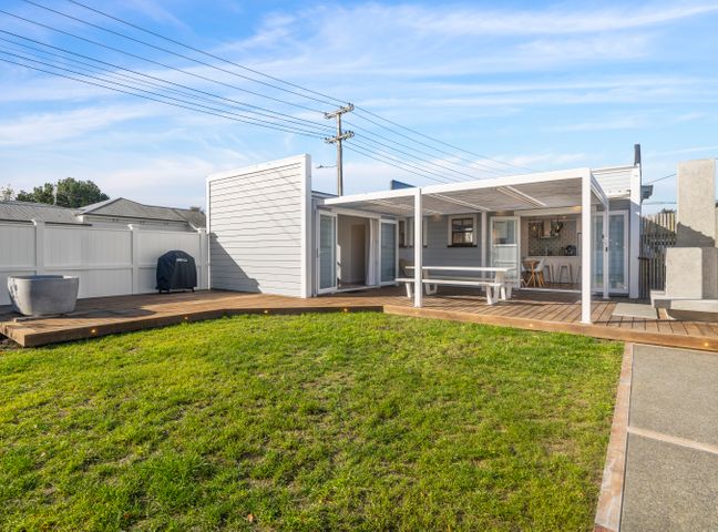 An outdoor patio with a covered seating area, wooden deck, grass lawn, barbecue grill, and a fenced yard at The Olive Corner- Martinborough Holiday Home