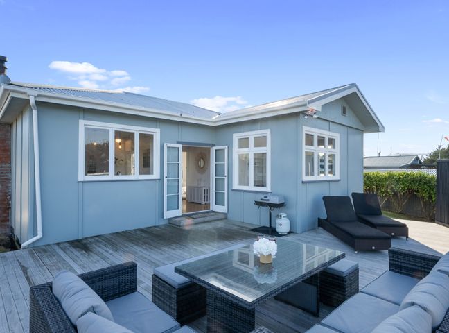 A patio area with outdoor seating furniture a glass table two lounge chairs and a barbecue grill at Ocean Breeze - Foxton Beach Holiday Home in Foxton Beach