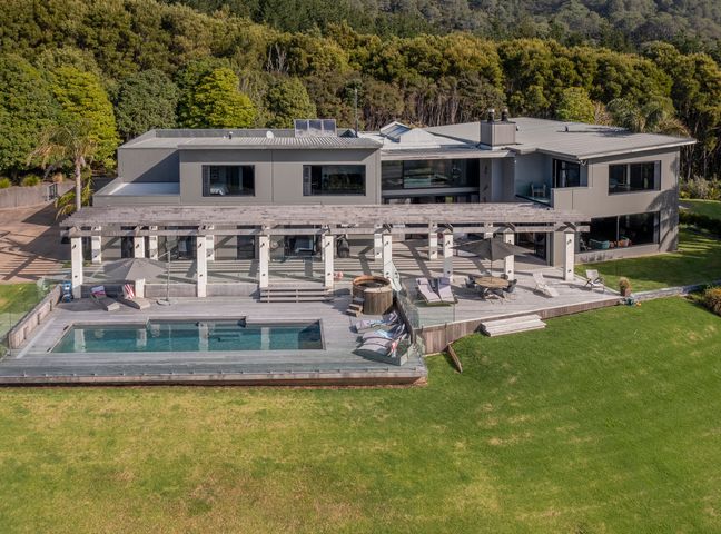 A large modern two-story house with a swimming pool patio seating and umbrella surrounded by green grass and trees at Te Punga Lodge Whangapoua Beach Luxury Villa Whangapoua 1.5km from Whangapoua Beach