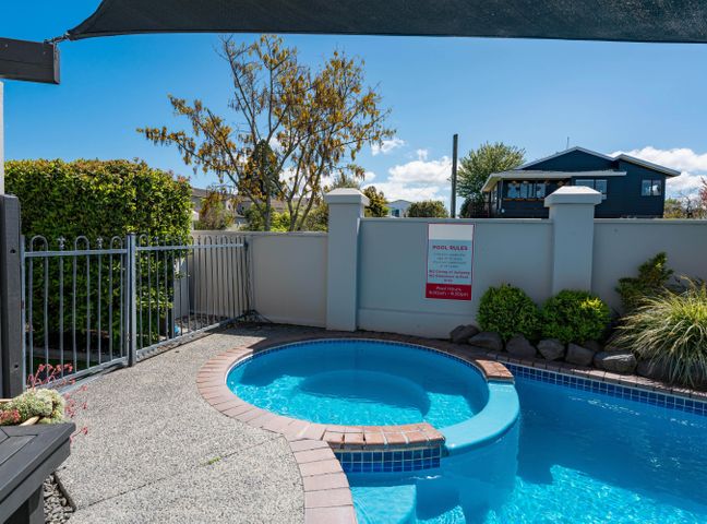 An outdoor pool area with a small round spa pool next to a larger pool surrounded by a concrete deck and metal fence at Sun and Swim - Lake Taupo Holiday Home Taupo Central