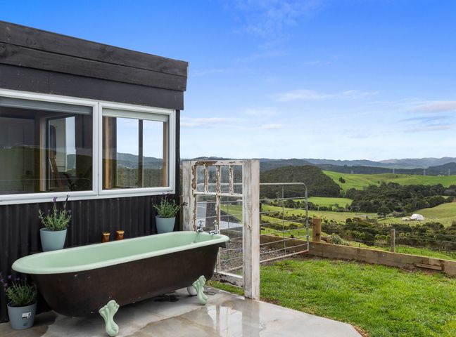 An outdoor bathtub next to a black building with a window and plants overlooking green hills and trees at Heart of Waipu Waipu