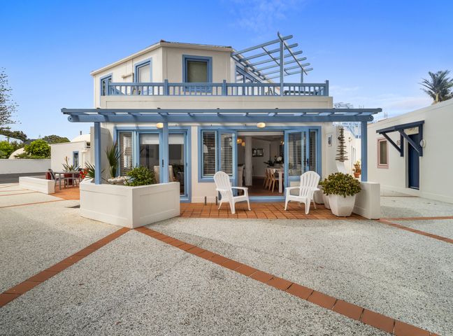 A two-story house with blue trim and patio chairs outside at Poolside Waterfront - Orewa Oceanside Villa in Orewa