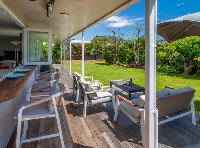 A covered outdoor deck with chairs and a table overlooking a grassy backyard at At The Beach - Pohara Holiday Home in Pohara Beach