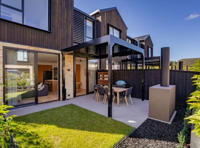 A backyard patio with a dining table and chairs under a pergola attached to a modern two-story house in Explorer's Rest Wanaka Holiday Home Wanaka